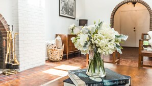 A room with a fireplace, a bookshelf with books, a vase with flowers, and a wooden door in the background.