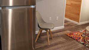 Una cuina moderna amb un frigorífic d'acer inoxidable, un televisor de pantalla plana al mur, una porta de fusta i una catifa colorida al terra.