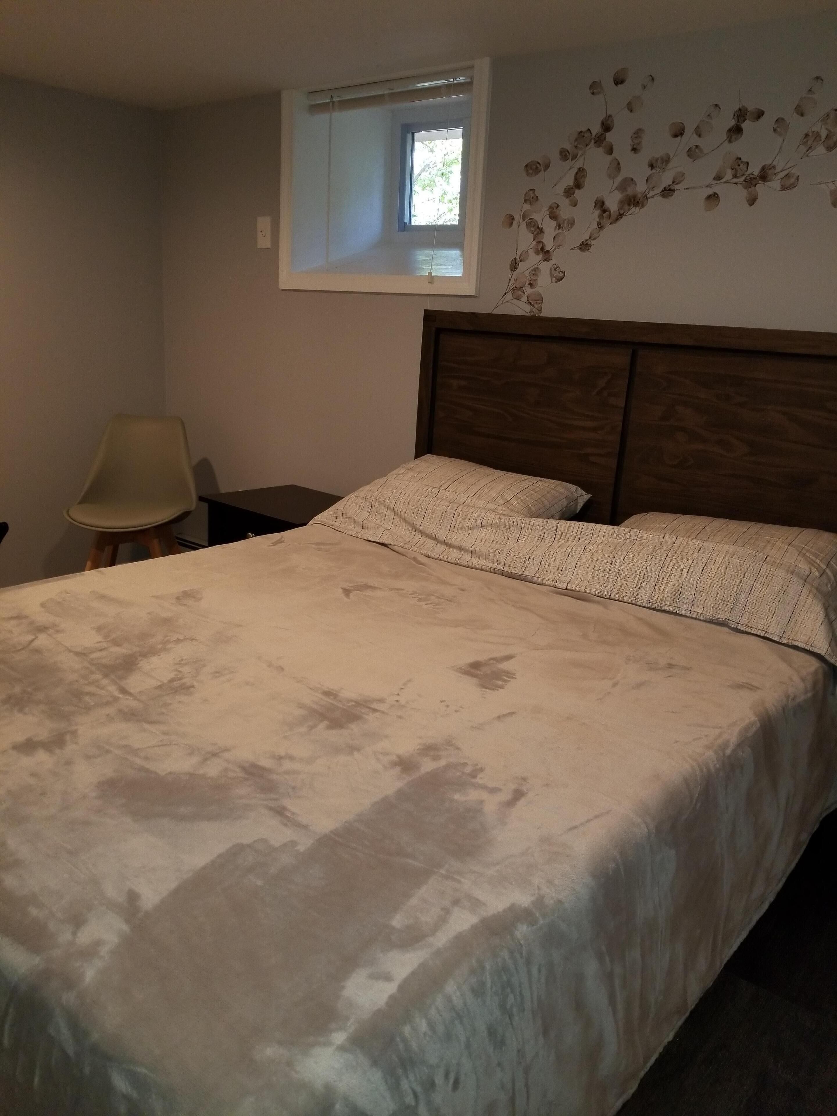 A bedroom with a bed, a nightstand, a chair, and a window with a view of trees.