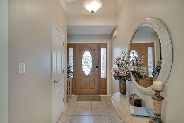 A hallway with a wooden door, a mirror, a vase with flowers, and a small table with a candle.