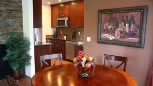 A dining area with a wooden table, chairs, a fruit centerpiece, a painting, and a kitchen in the background. - Model 3 Bedrm with office/den  second floor with stunning mountain views (Tucson)