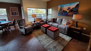 A living room with a sofa, armchairs, a coffee table, and a rug. There is a ceiling fan, a painting on the wall, and a window with a view of the outside. - Model 3 Bedrm with office/den  second floor with stunning mountain views (Tucson)