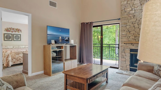 Una sala de estar con una mesa de centro de madera, sofás color beige, un televisor y una chimenea de piedra.