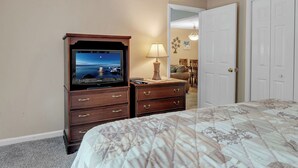 Un dormitorio con una cama, un televisor sobre un tocador de madera y una puerta.