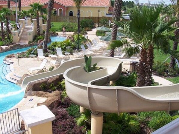 A pool area with a water slide, lounge chairs, and palm trees.