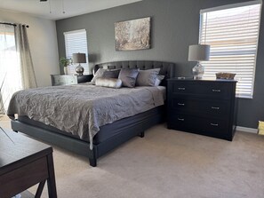 A bedroom with a large bed, a nightstand, a dresser, and a window with blinds.
