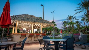 An outdoor bar area with a thatched roof, bar stools, and tables. - Elite end unit, sleeps 10, 5 min walk to pool, many extras. Close to Disney. (Davenport)