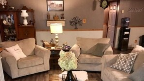 Ett vardagsrum med två beige soffor, ett soffbord i trä med en vas med blommor och en matta på golvet.
