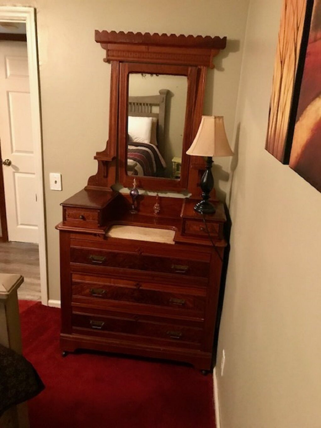 Een houten dressoir met spiegel, een lamp en een rode tapijt.
