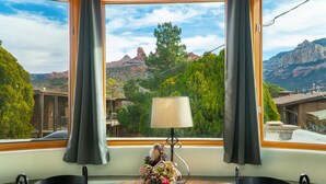 A room with a view of a mountainous landscape through large windows, a small table with a lamp, and a decorative item. - Walk a Block to Uptown, to the main shops, tours, restaurants. (Sedona)