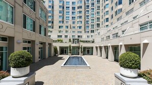 Ein modernes Gebäude mit einem zentralen Innenhof, das ein rechteckiges Schwimmbecken, Kübelpflanzen und mehrere Balkone zeigt.