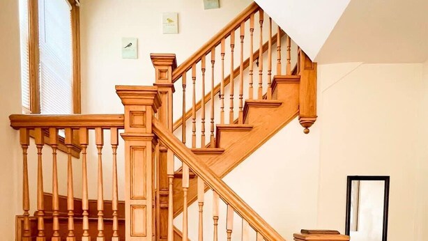 A wooden staircase with a curved design, flanked by wooden handrails and a wooden baseboard. - After the Game Apt 1 - All Star Baseball Rentals (Oneonta)