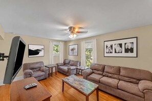 A living room with a ceiling fan, leather sofas, a coffee table, and artwork on the walls. - After the Game Apt 1 - All Star Baseball Rentals (Oneonta)