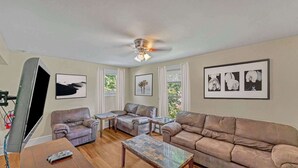 A living room with a sofa, two armchairs, a coffee table, and a TV. There are framed pictures on the wall and a ceiling fan. - After the Game Apt 1 - All Star Baseball Rentals (Oneonta)