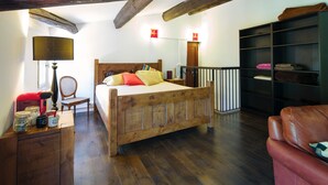 Ein Bett mit Holzkopfteil, ein Nachttisch mit Lampe, ein Stuhl und ein Bücherregal.