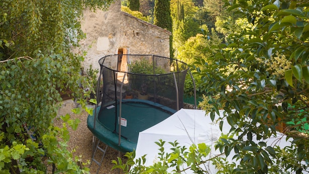 Ein Garten mit Trampolin, umgeben von üppigem Grün und einer Steinmauer.