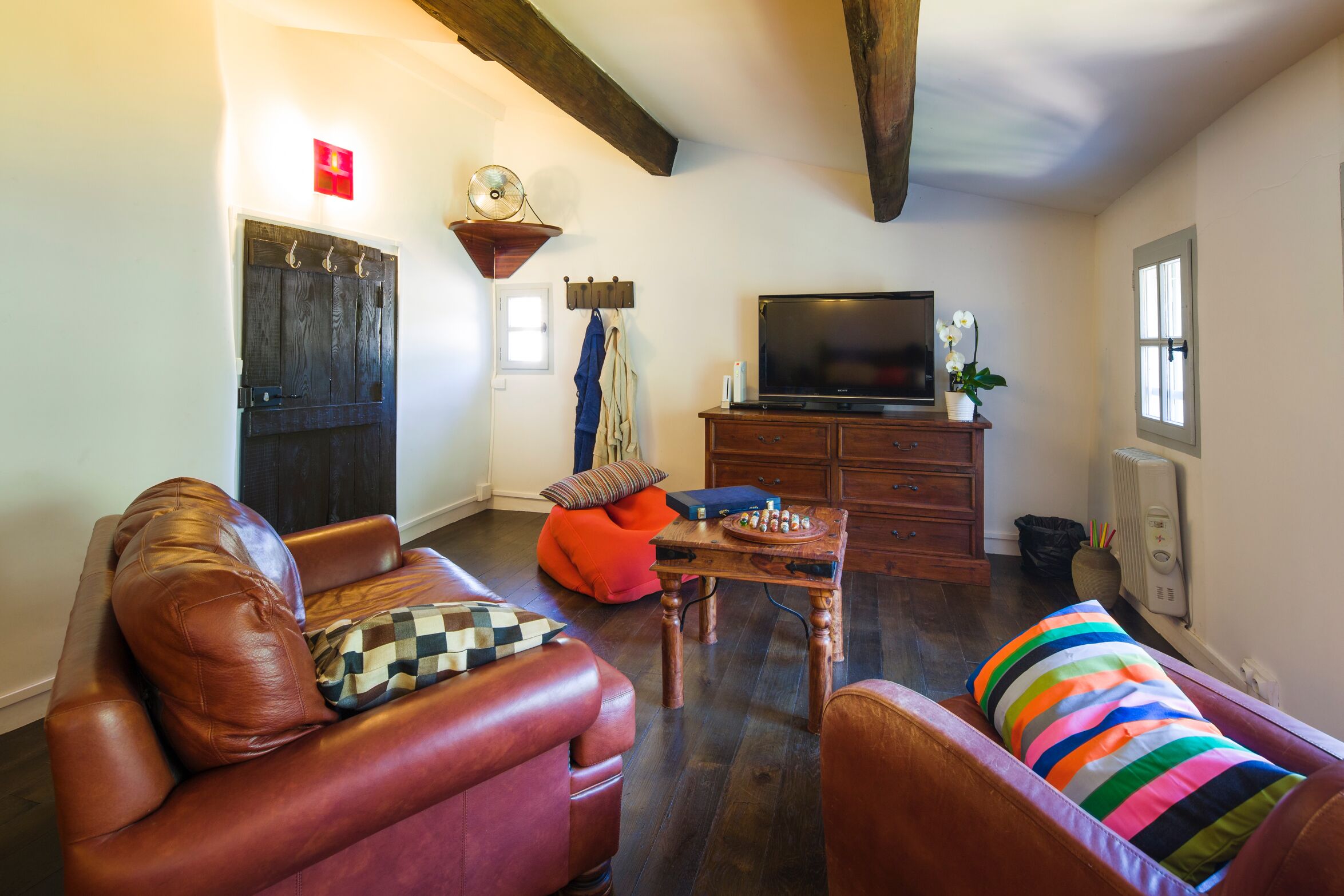 A living room with a brown leather sofa, a striped cushion, a wooden coffee table, and a television on a wooden cabinet.