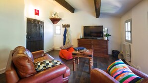 Ein Wohnzimmer mit einem braunen Ledersofa, einem gestreiften Kissen, einem Holztisch und einem Fernseher auf einer Holzkommode.