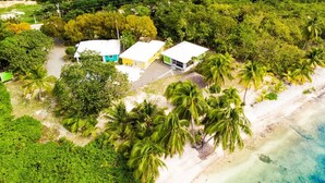 Vista aérea de una propiedad costera con tres edificios separados, una playa de arena y exuberante vegetación tropical.