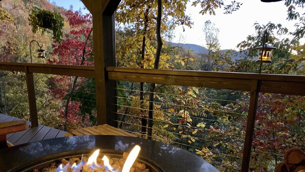 Bocca di fuoco con fiamme, un pontile in legno e vista sulla vegetazione autunnale e sulle colline.