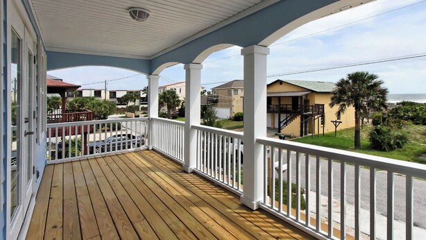 Um deck de madeira com grades brancas, uma área coberta com teto e vista para casas e uma palmeira.