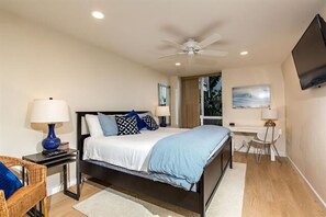 A bedroom with a bed, two bedside tables, a chair, a desk, a ceiling fan, a TV, and a window.