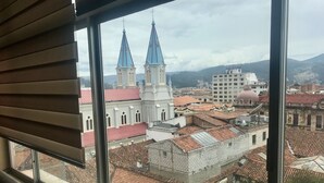 A view from a window overlooking a historic building with two spires and a red-tiled roof.