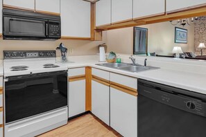 Compact kitchen with a stove, oven, microwave, and dishwasher, featuring white cabinetry and a wooden floor.