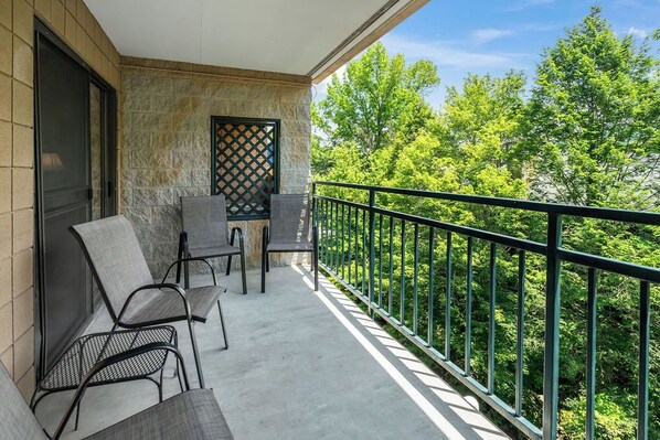 Relax on the balcony with a serene view of lush greenery, featuring a comfortable seating area with two chairs and a table.