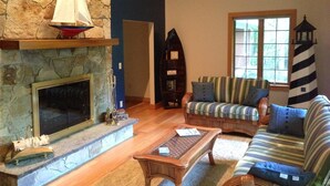 A cozy living room with a stone fireplace, a striped sofa, and a wicker coffee table. - Booking now Winter Rental Sept 2026-May 2027. Please message for monthly prices (Kennebunkport)