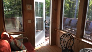 A wooden deck with a red sofa and a wicker chair, a small round table, and a view of a deck chair area through a glass door. - Booking now Winter Rental Sept 2026-May 2027. Please message for monthly prices (Kennebunkport)