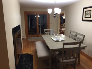 A dining area with a wooden table, chairs, a bench, a chandelier, and a fireplace.