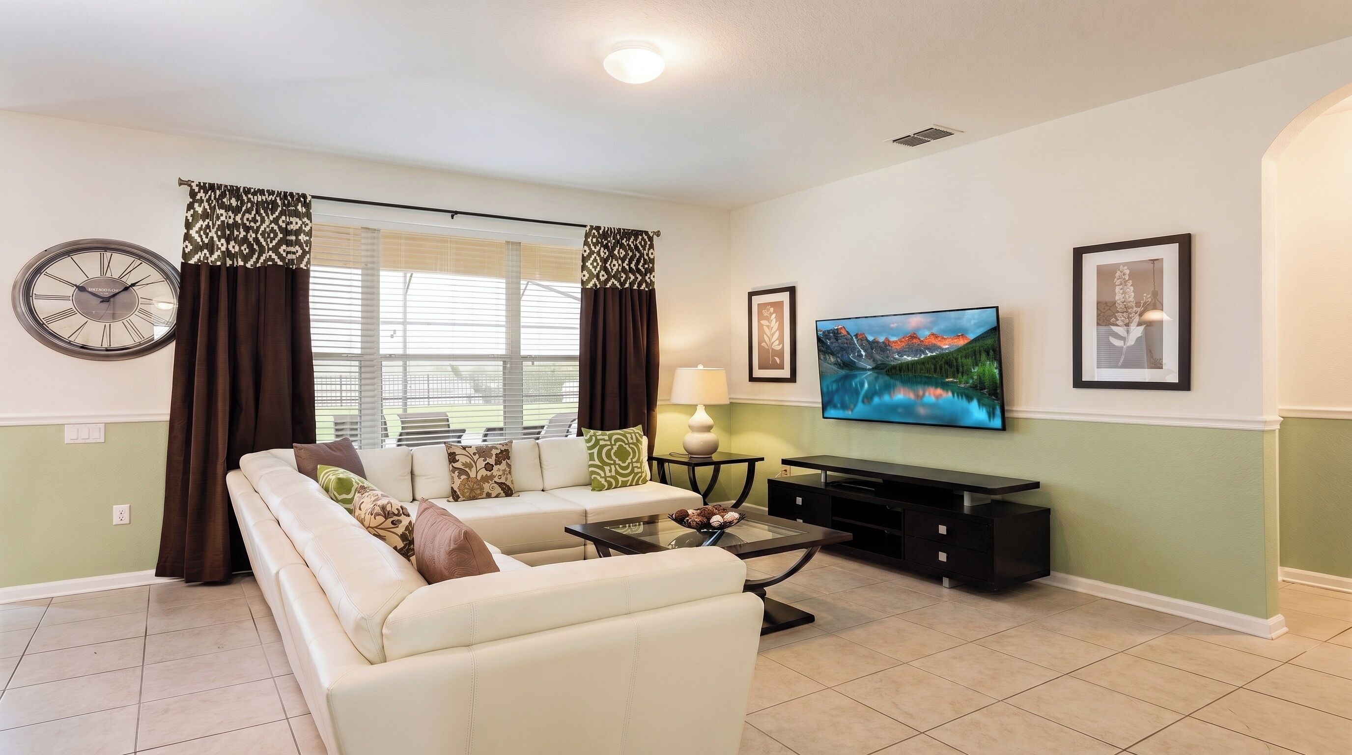 A living room with a sofa, a coffee table, a TV, and a clock on the wall.