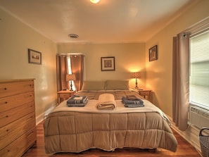 A bedroom with a bed, wooden dresser, nightstands, lamps, and a window with curtains.