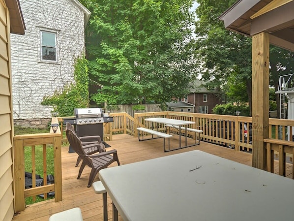 A deck with a grill, wooden chairs, and a table.