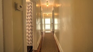 A narrow hallway with a patterned shower curtain, a thermostat on the wall, and a ceiling light.