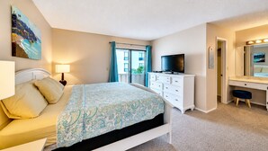 A bedroom with a bed, a dresser, a TV, and a bathroom mirror. - 2 bedroom, 3 beds, 2 1/2 bath Duplex on Siesta Key • Heated Pool & Fishing Dock (Siesta Key)