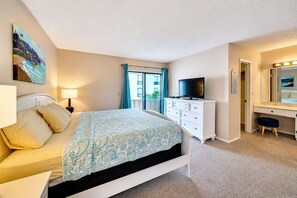 Ein Schlafzimmer mit einem Bett, einem Schminktisch, einem Fernseher und einem Badezimmerspiegel.