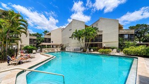 A swimming pool with lounge chairs and palm trees, surrounded by buildings with balconies. - 2 bedroom, 3 beds, 2 1/2 bath Duplex on Siesta Key • Heated Pool & Fishing Dock (Siesta Key)