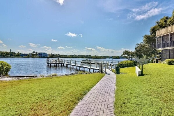 A waterfront property with a paved walkway, a dock, and a building with large windows. - Siesta Key Beach • 2BR, 3 beds, 2 1/2 bath Duplex • Heated Pool & Fishing Dock (Siesta Key)