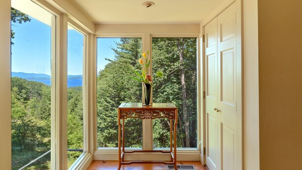Quarto com grandes janelas que oferecem vista para uma floresta e montanhas.