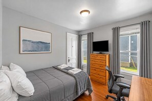 Une chambre à coucher avec un lit, une commode, un téléviseur et une fenêtre avec des rideaux.