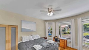 A bedroom with a bed, a desk, and a view of the street through large windows. - After the Game Apt 2 - All Star Baseball Rentals (Oneonta)