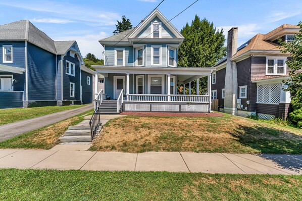 A two-story house with a front porch, a small front yard, and a sidewalk leading to the street.