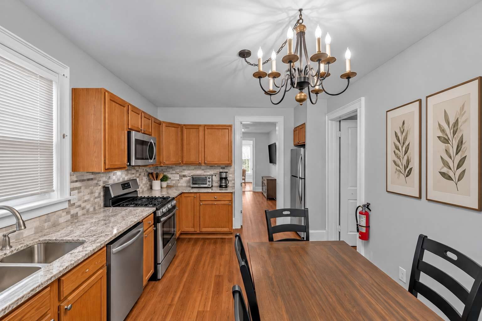 A modern kitchen with wooden cabinets, a granite countertop, stainless steel appliances, and a dining area with a wooden table and chairs.