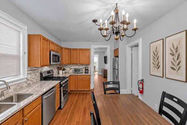 A modern kitchen with wooden cabinets, a granite countertop, stainless steel appliances, and a dining area with a wooden table and chairs.