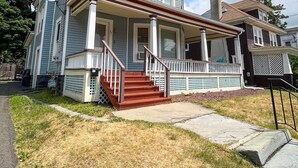 A two-story house with a front porch, a satellite dish, and a visible air conditioning unit. - After the Game Apt 2 - All Star Baseball Rentals (Oneonta)
