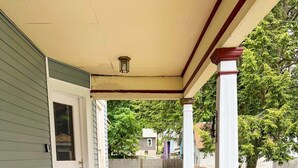 A covered porch with a red floor, white railings, and a wooden fence in the background. - After the Game Apt 2 - All Star Baseball Rentals (Oneonta)