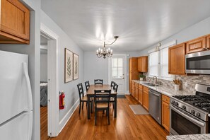 Une cuisine avec des meubles en bois, une cuisinière en acier inoxydable et un coin repas comprenant une table et des chaises.