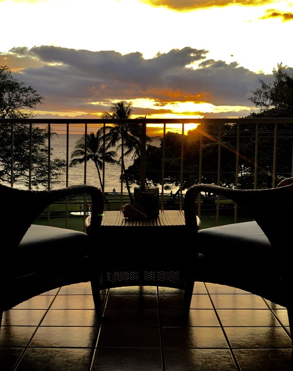 Un balcón con vista al atardecer sobre el mar, con una silla y una mesa.